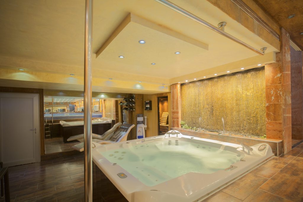 Luxury hotel suite with a private hot tub, ambient lighting, spa loungers, and indoor relaxation area